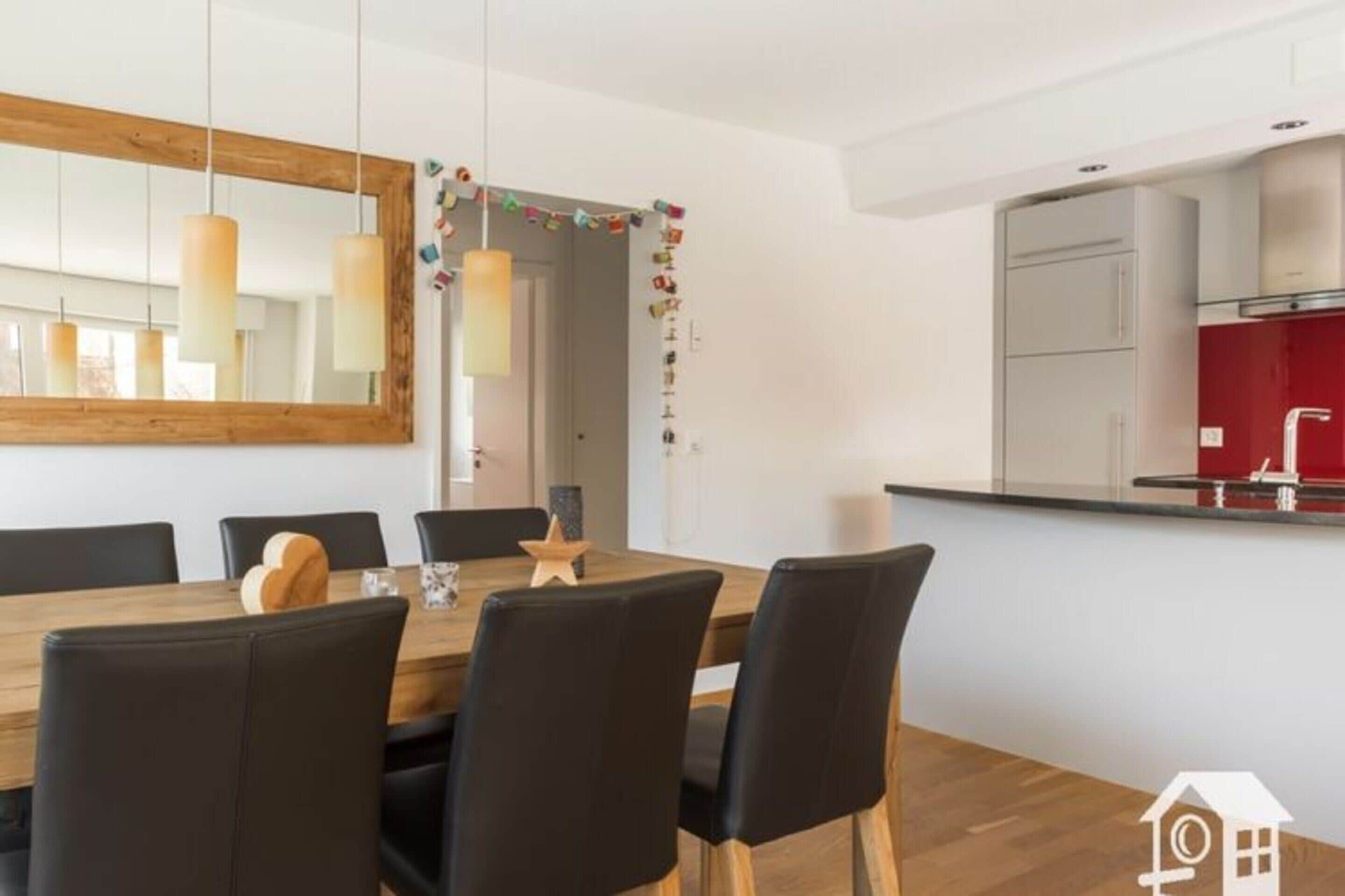 Uma cozinha moderna com uma geladeira vermelha, uma mesa de jantar de madeira com cadeiras pretas e uma luminária pendente.