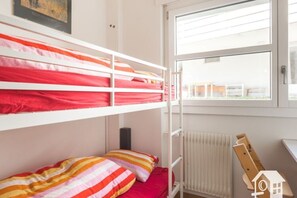 Ein Schlafraum mit Etagenbetten, einem Fenster, einer Heizung und einem Holzstuhl.