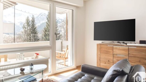 Un salon moderne doté d’une grande fenêtre, d’un téléviseur à écran plat, d’un canapé en cuir et d’un meuble en bois.