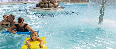 A pool with a water fountain, lounge chairs, and a rock feature.