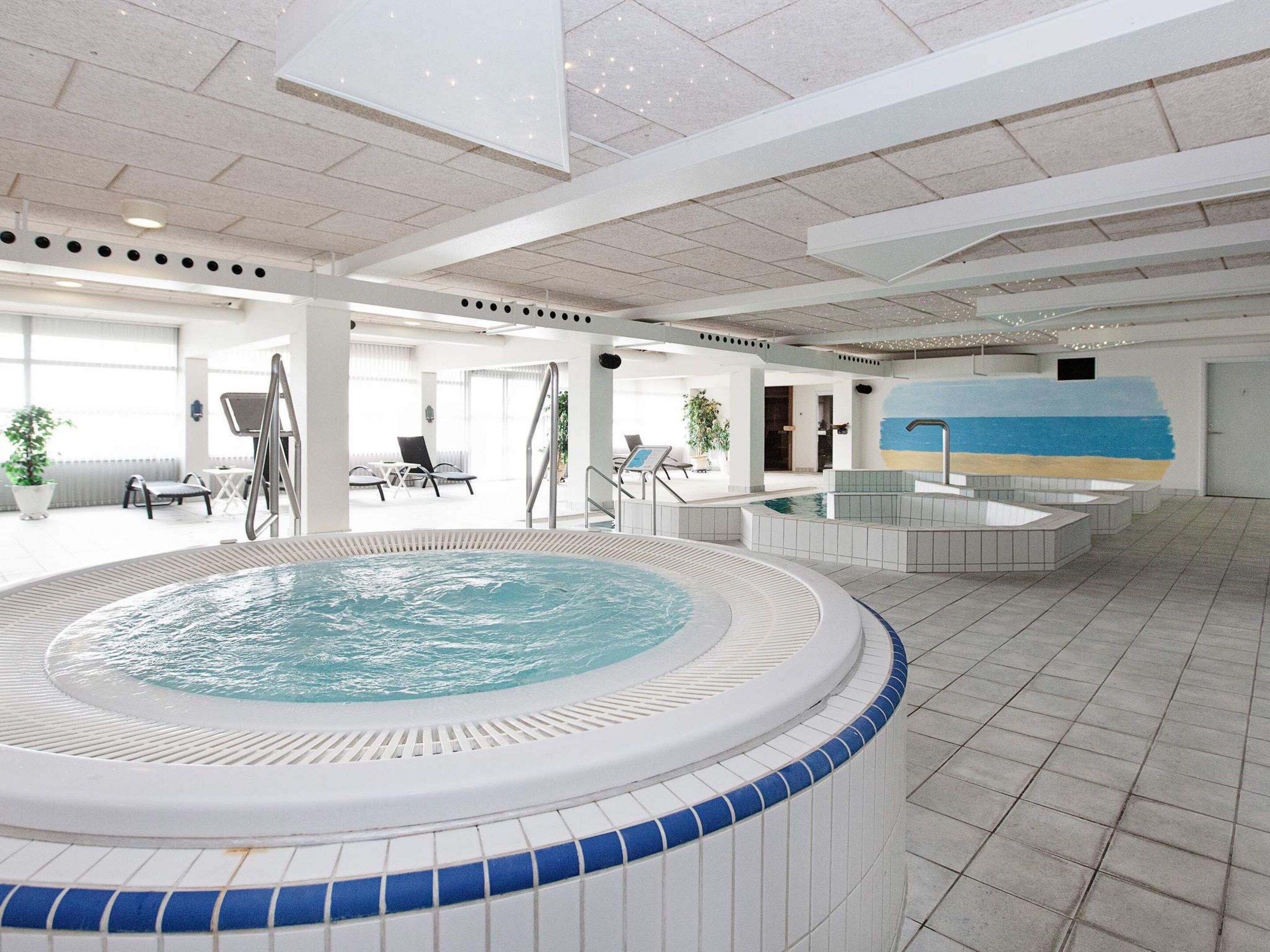 Una amplia piscina interior con un jacuzzi, sillas de descanso y un mural en la pared.