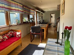 A cozy dining area with a wooden table and chairs, a sofa with patterned cushions, and a window with striped curtains.