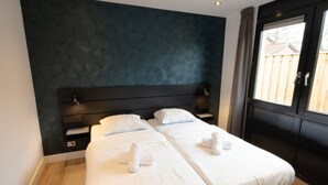 Un lit double avec du linge de lit et des serviettes blanches, une tête de lit sombre et une fenêtre avec des rideaux.
