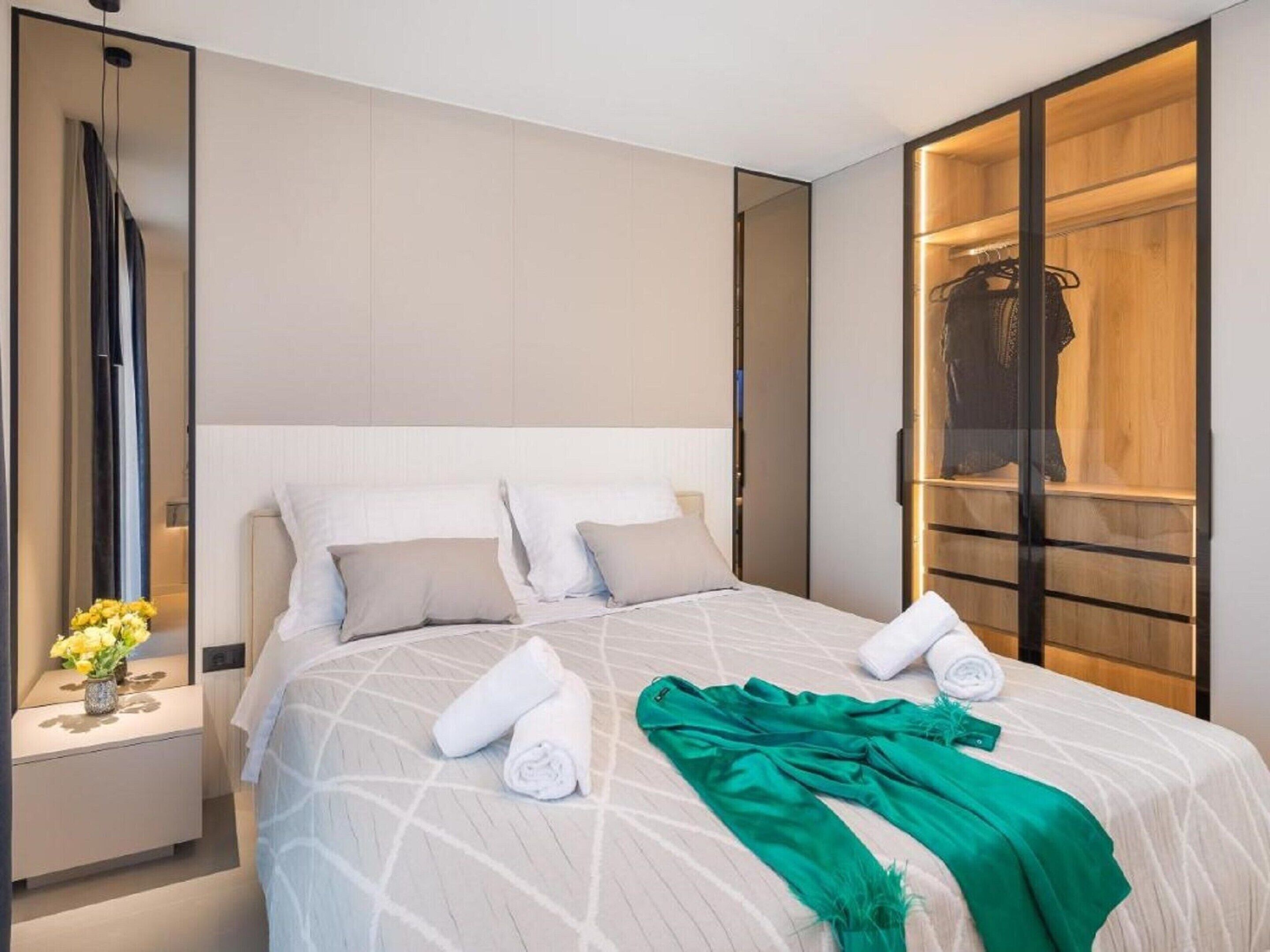 A modern hotel room with a large bed, a nightstand with a vase of flowers, and a wooden wardrobe.