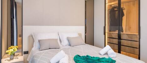 A modern hotel room with a large bed, a nightstand with a vase of flowers, and a wooden wardrobe.