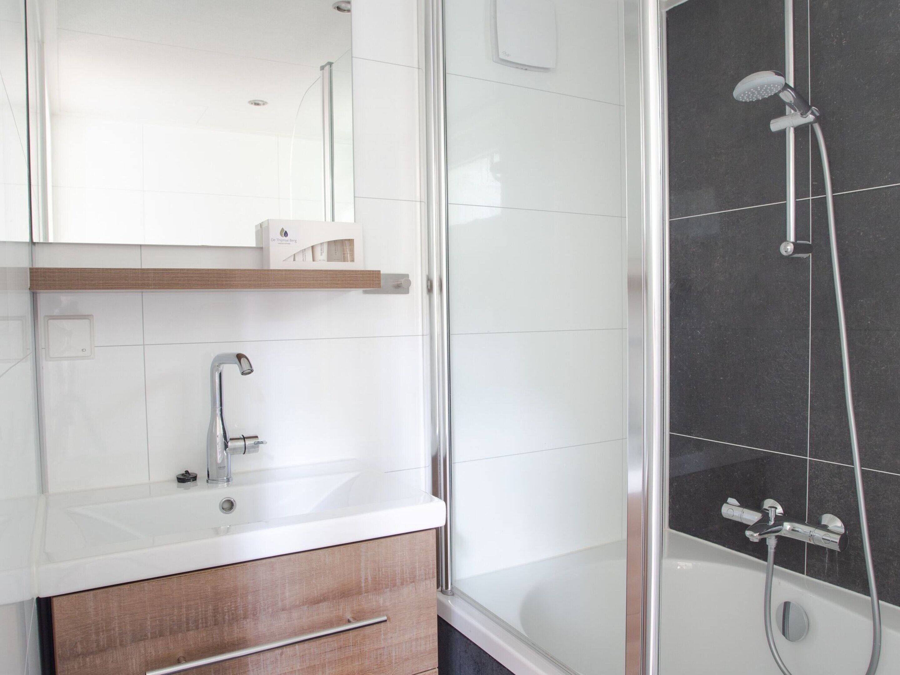 A modern bathroom with a white vanity, a mirror, a shower with a handheld showerhead, and a bathtub.