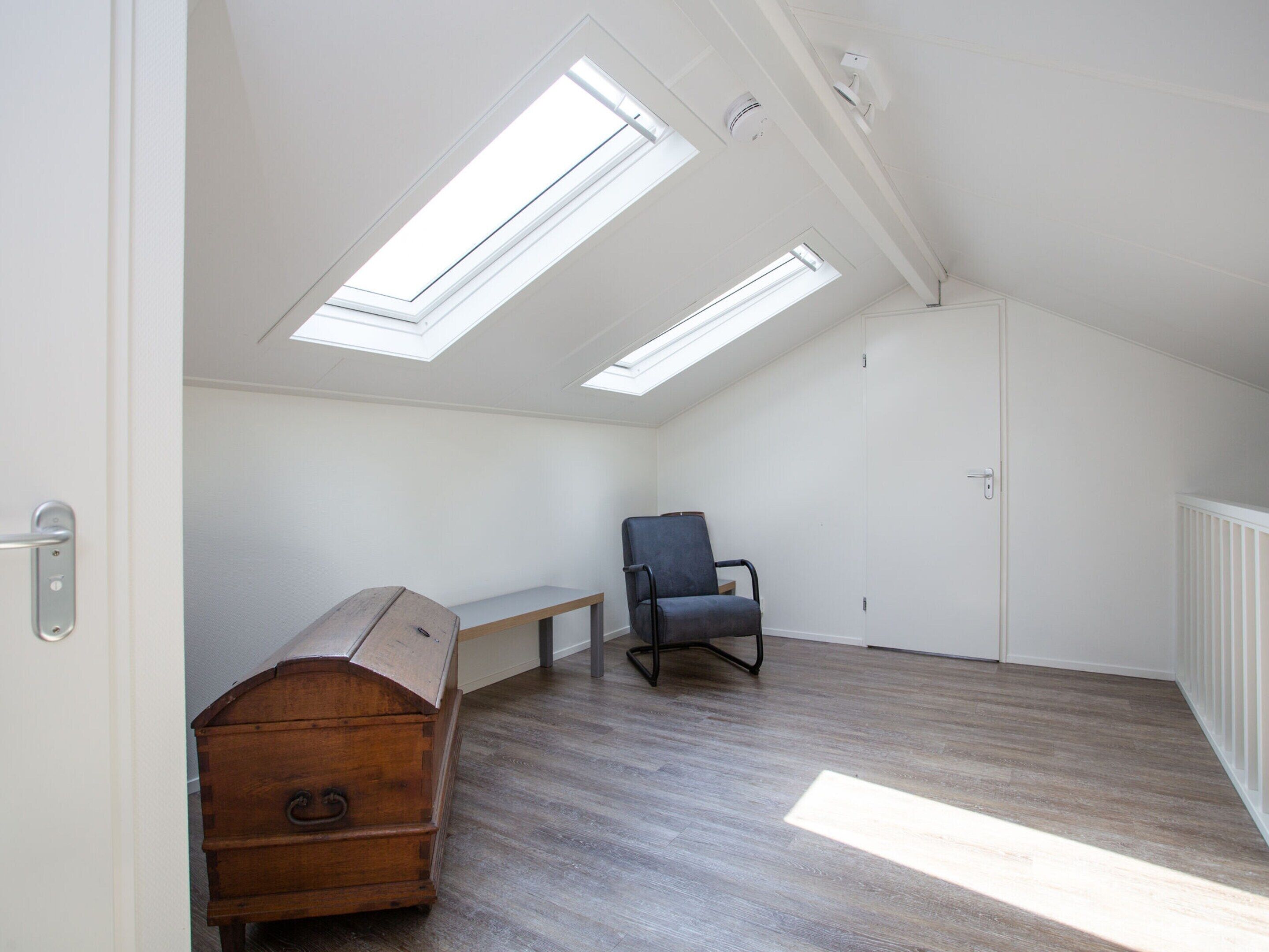 A high-ceilinged room with skylights, a wooden chest, a bench, and a chair.