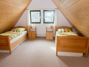 Un dormitorio en el ático, pequeño, con dos camas de madera, una ventana y un radiador.