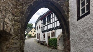 A cobblestone street leading through a stone archway to a traditional half-timbered building with a white facade and black timber framing. - Mechthild and Hans-jurgen Geschwind (Schleiden)