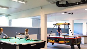 Ein Billardtisch mit Kugeln und ein kleinerer Tisch in einem Raum mit großen Fenstern und einem Deckenventilator.