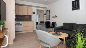 Ein zeitgemäßer Wohnraum mit grauem Sofa, einem kleinen runden Tisch und einer Küchenzeile mit Holzschränken und integriertem Backofen.