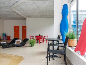 A modern lounge area with red and black chairs, a small table, and a large blue sculpture.