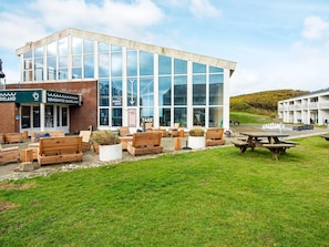 A modern building with a glass facade, outdoor seating area with wooden benches, and a chessboard on the ground.