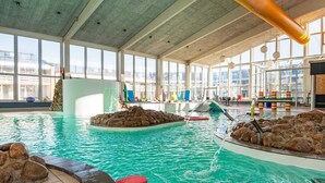 Una piscina interior con agua cristalina, formaciones rocosas y una zona de juegos para niños.