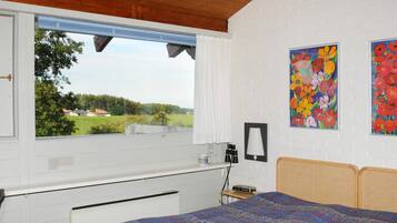 Quarto com cama, janela com vista para o verde, radiador e duas pinturas na parede.