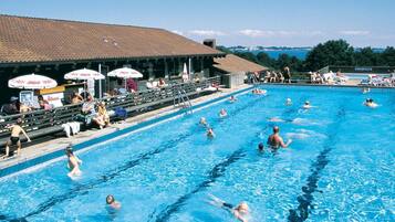 Una piscina con varias pistas de natación, espectadores y sombrillas.