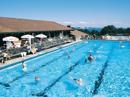 Una piscina con diverse corsie, spettatori e ombrelloni.