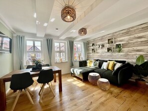 A modern living room with a wooden floor, a sofa set, a dining table with chairs, and a TV mounted on the wall. - Modern Holiday Home in the Center (Wernigerode)