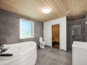 A modern bathroom with a large bathtub, a toilet, and a shower area. - 5 Star Holiday Home in Henne (Henne)
