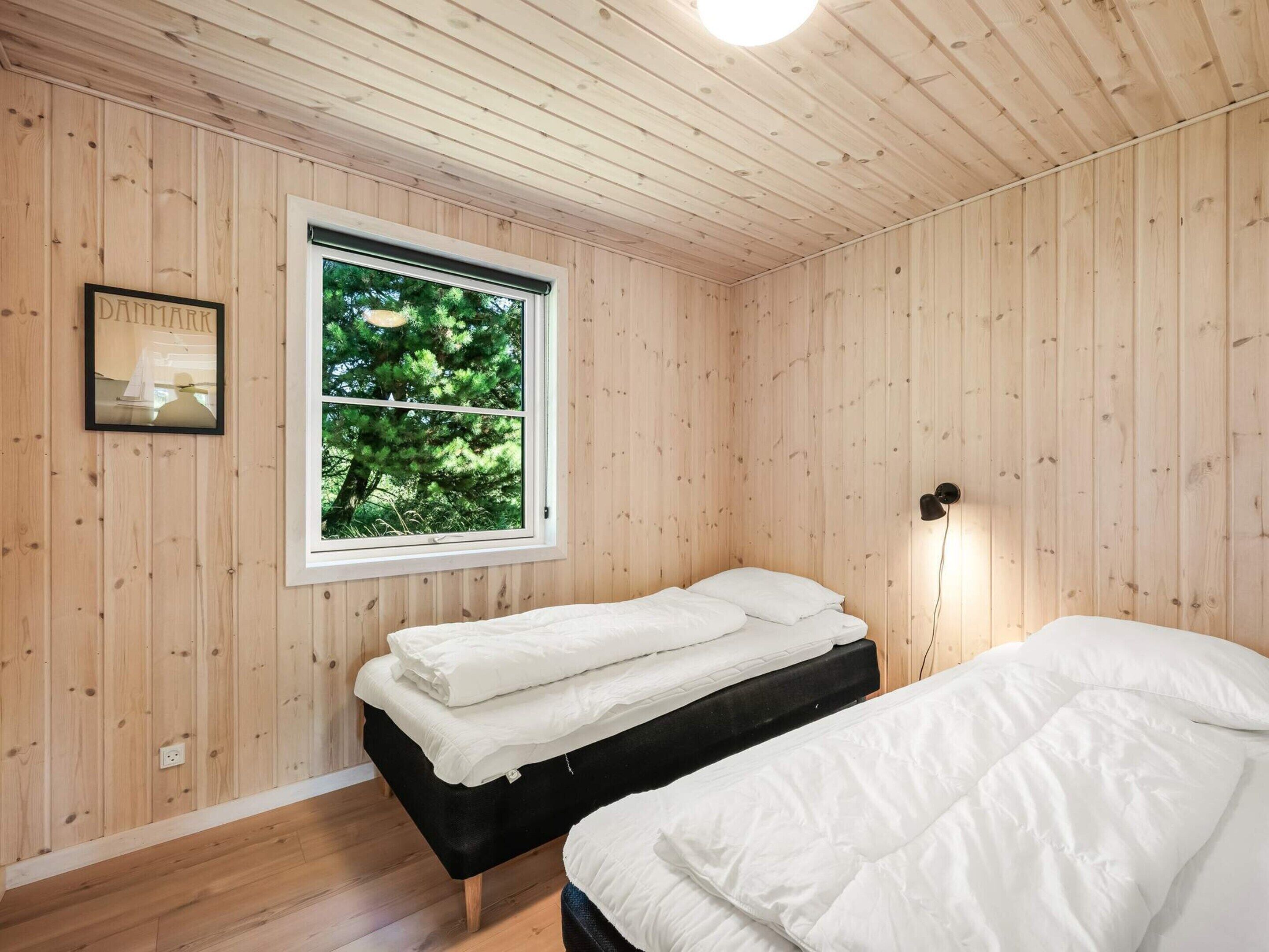 A room with wooden walls and a window with a view of trees. There is a bed with white bedding and a black headboard.
