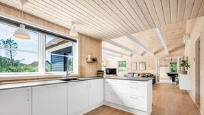 A modern kitchen with white cabinetry, a central island, and a large window offering a view of the outdoors. - 5 Star Holiday Home in Henne (Henne)