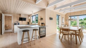 A modern kitchen with wooden accents, a central island with stools, and a dining area with a large table and chairs. - 5 Star Holiday Home in Henne (Henne)