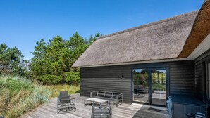En moderne udendørs terrasse med stråtæthed, møbleret med metalstole og et bord, omgivet af vegetation.