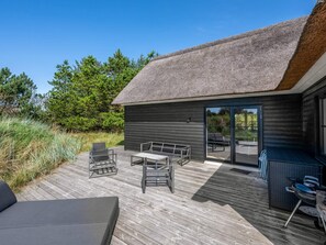 A modern outdoor deck with a thatched roof, furnished with metal chairs and a table, surrounded by greenery. - 5 Star Holiday Home in Henne (Henne)