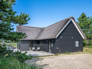 Ett modernt hus med en mörk fasad, ett sluttande tak och en liten veranda med två stolar.