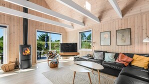 A modern living room with a fireplace, leather sofa, and large windows. - 5 Star Holiday Home in Henne (Henne)