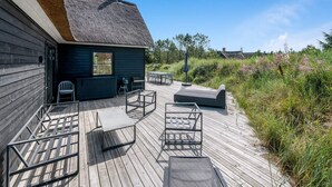 En træterrasse med udendørs møbler og en bygning med stråtak.