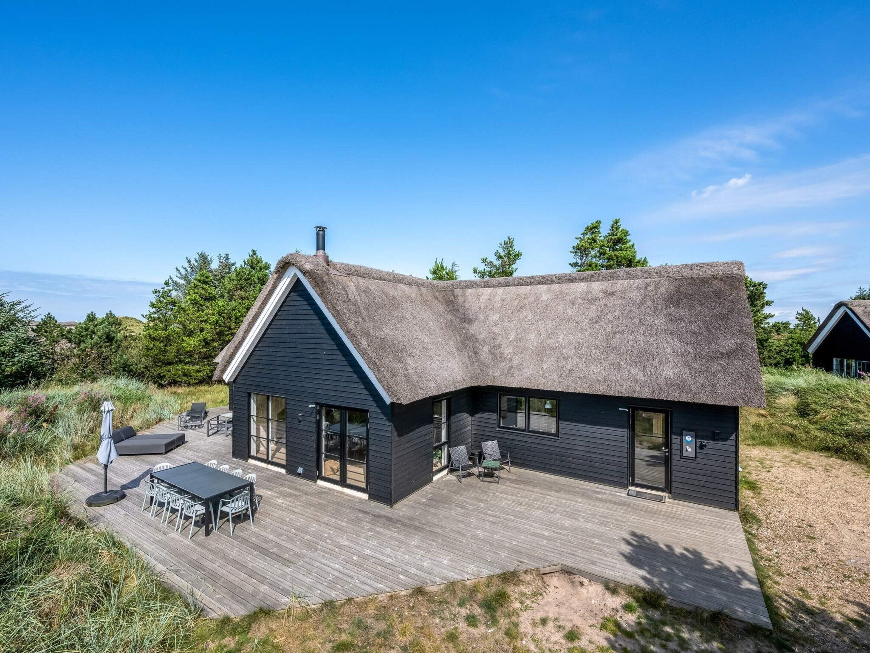 Una casa moderna con techo de paja, grandes ventanales y una terraza con mobiliario exterior.