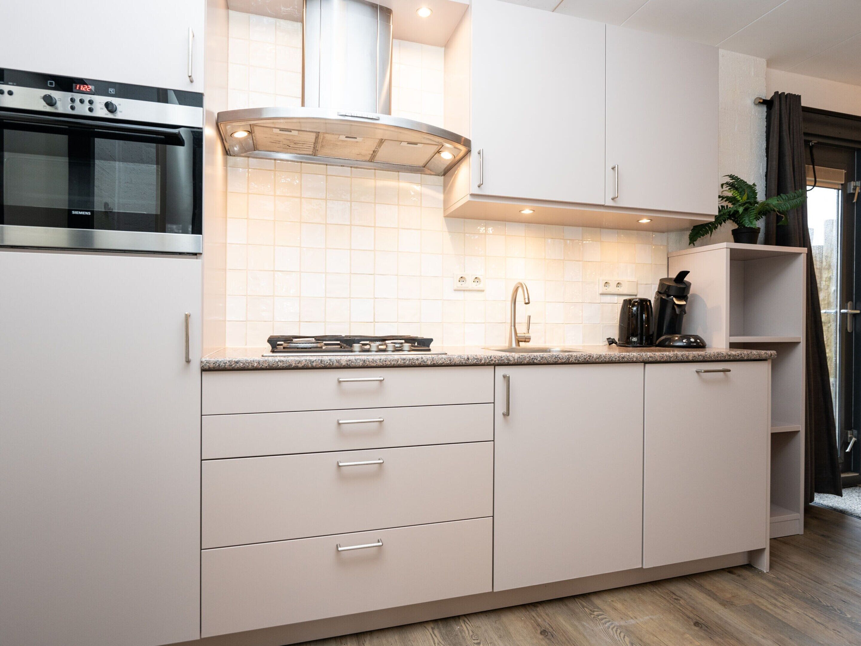 A modern kitchen with white cabinetry, a stainless steel oven, a gas stove, and a built-in range hood.