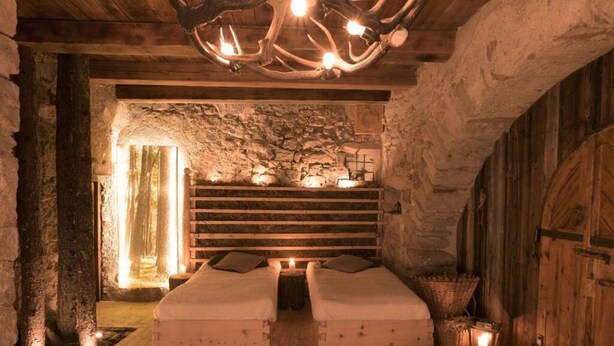 Une pièce rustique aux murs de pierre, avec un lit en bois, un mur en pierre et un plafond en bois.