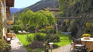 Un jardin avec un sentier en pierre, un espace aménagé avec une table et des chaises, un petit étang et une vue sur une montagne.