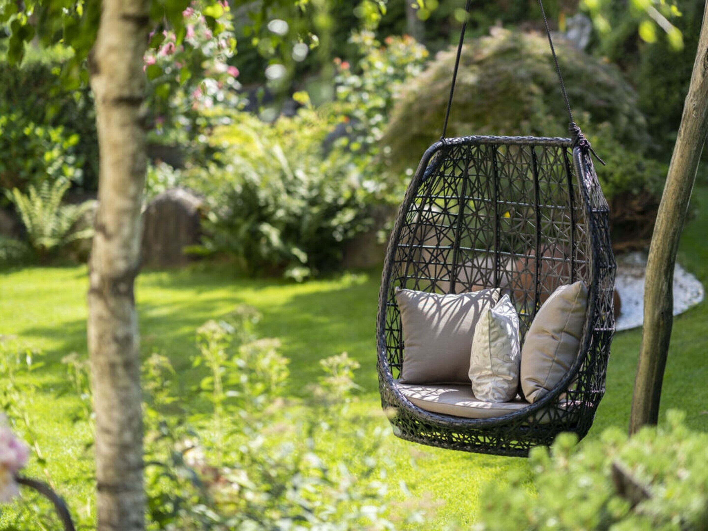 Una silla colgante con cojines en un jardín exuberante.