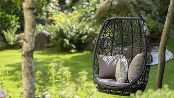 Una silla colgante con cojines en un jardín exuberante.