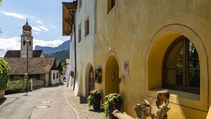 Une rue étroite bordée d’immeubles jaunes, une église dotée d’un clocher et un banc en bois.