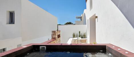 A rooftop pool with a stone wall and a table with chairs.