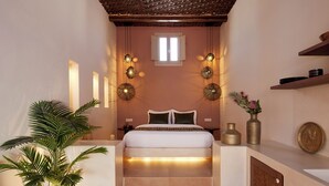 Un dormitorio con cama, mesitas de noche, una planta en maceta y una ventana.