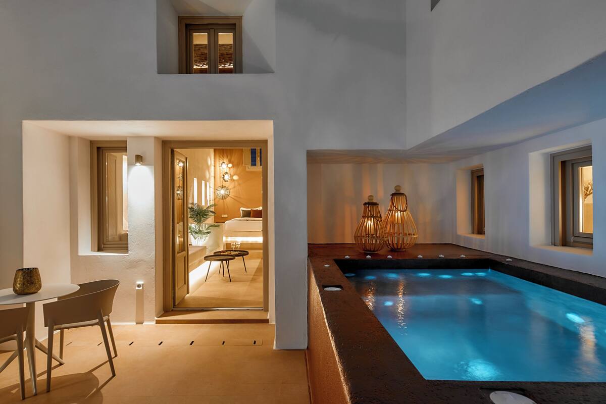 A modern indoor pool area with a clear view of the adjacent living room, a dining area, and a staircase leading to an upper level.