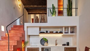 Un interior moderno con una escalera, un balcón con plantas y una zona de estar con una mesita de centro.