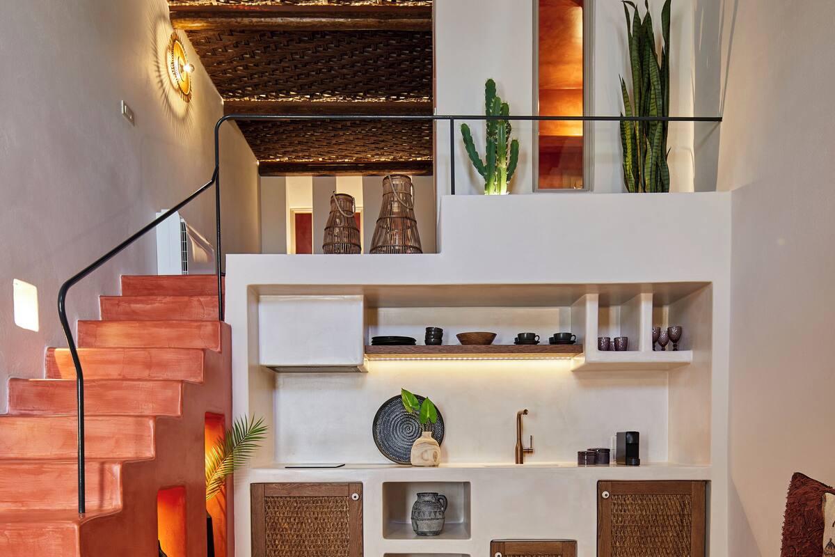 A modern interior with a staircase, a balcony with plants, and a seating area with a coffee table.