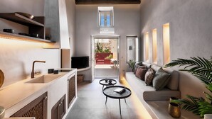 Un pasillo estrecho con una zona de cocina a un lado y una sala de estar al otro. Hay dos pequeñas mesas redondas, un sofá y un televisor en un estante.