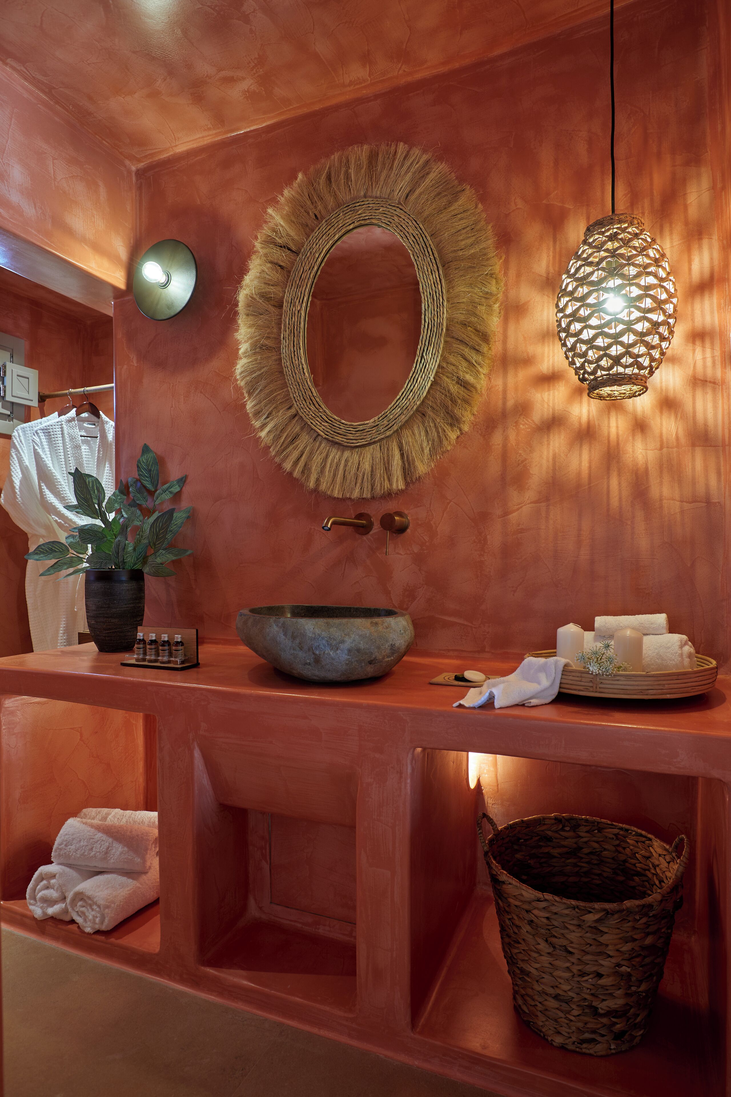 A bathroom with a large mirror, a round woven mirror frame, a stone basin, a potted plant, a hanging light fixture, and a woven basket.