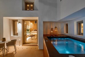 A modern indoor swimming pool with a view of a cozy room and a dining area. - DOMUS HESTIA SUITES (Santorini)