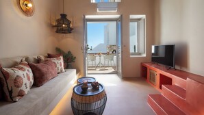 Una sala de estar moderna con un sofá, una televisión y un comedor visibles a través de la puerta de vidrio.