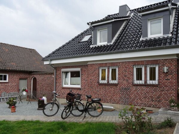 A two-story brick house with a tiled roof, two bicycles parked in front, and a small garden area. - Rose Comfortable Holiday Residence (Kappeln)