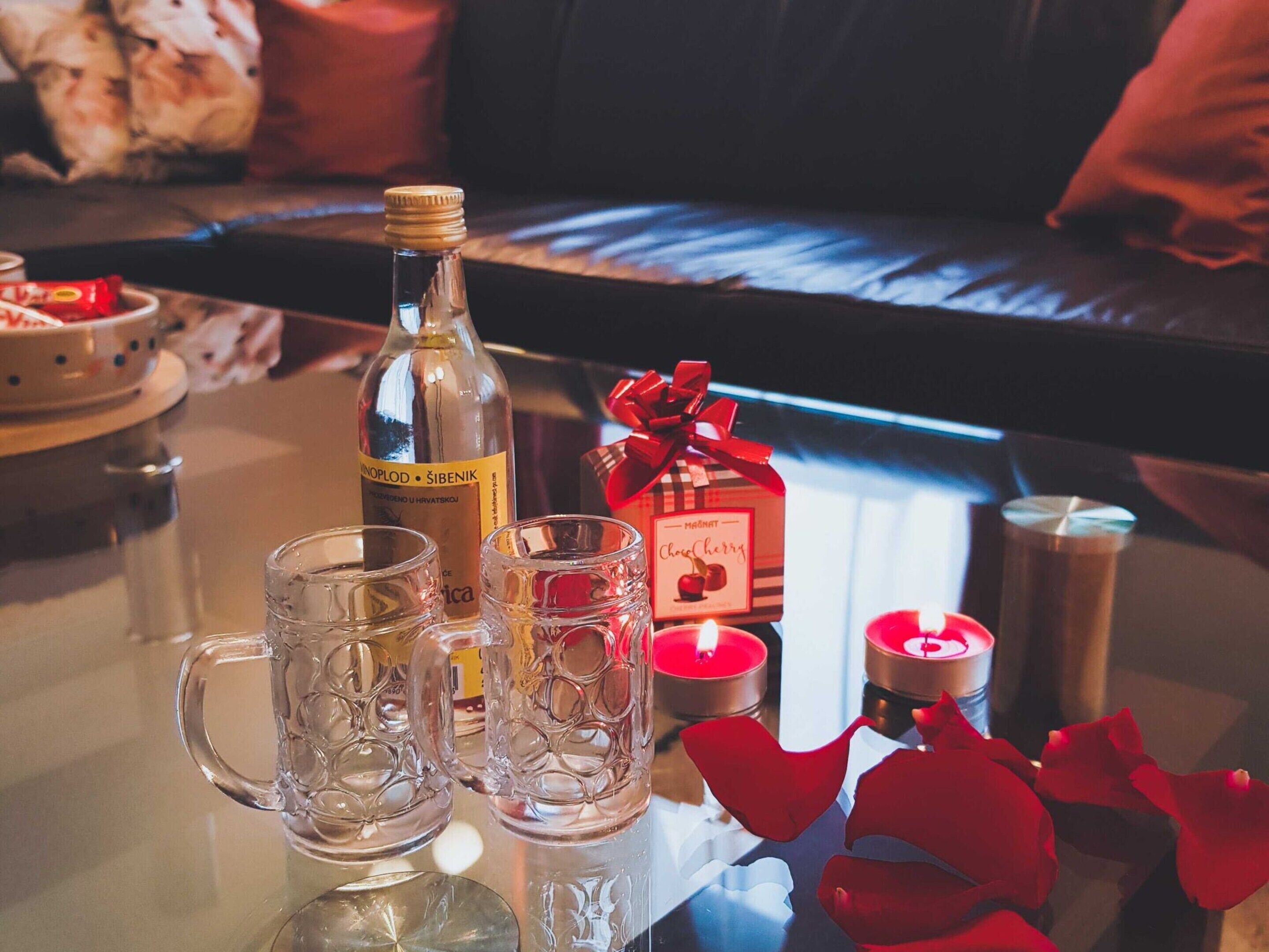 Una mesa con una botella, dos vasos, una vela y una caja de regalo.