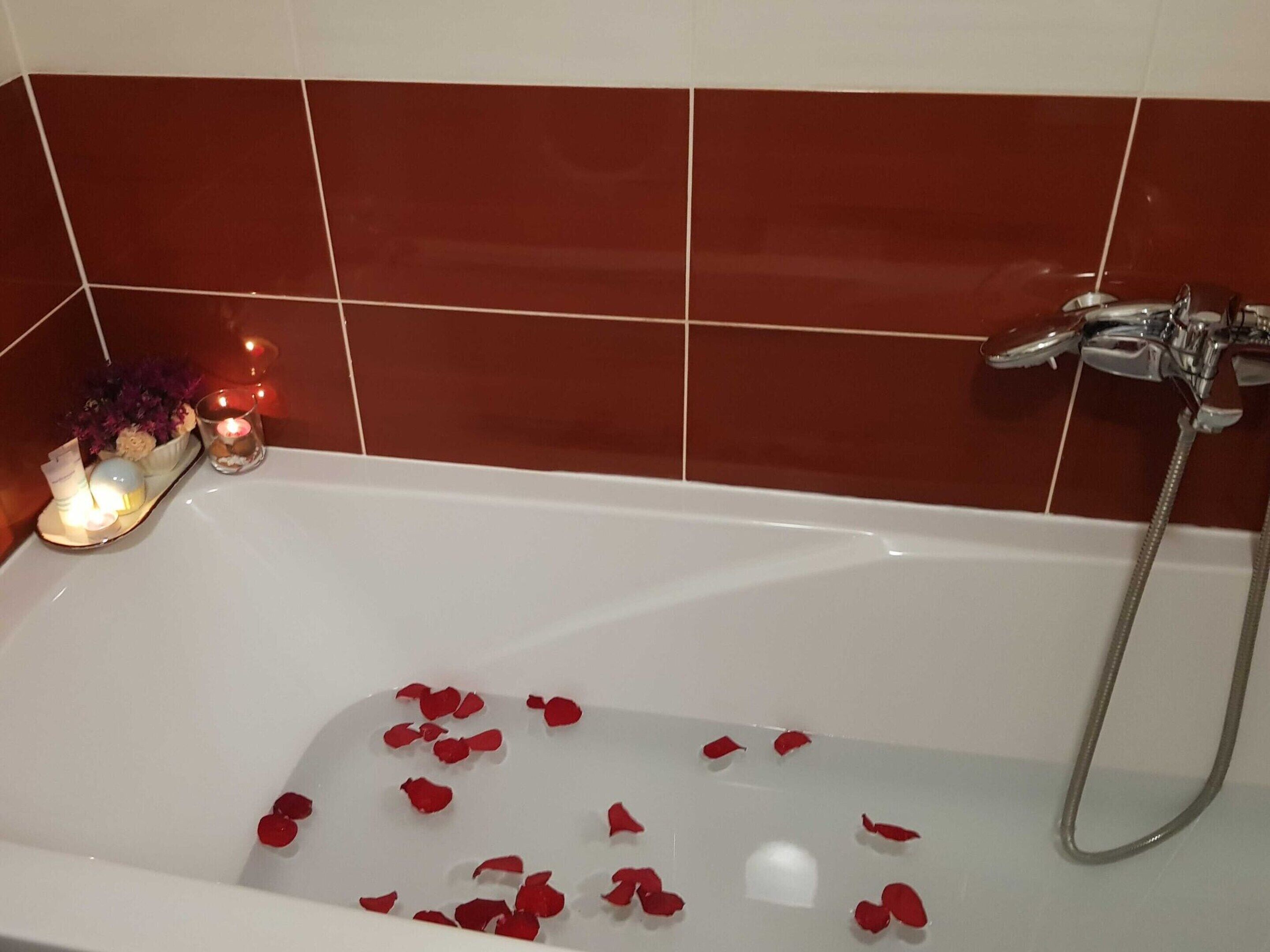 Una vasca da bagno con petali di rosa e candele, che evoca un'atmosfera romantica.